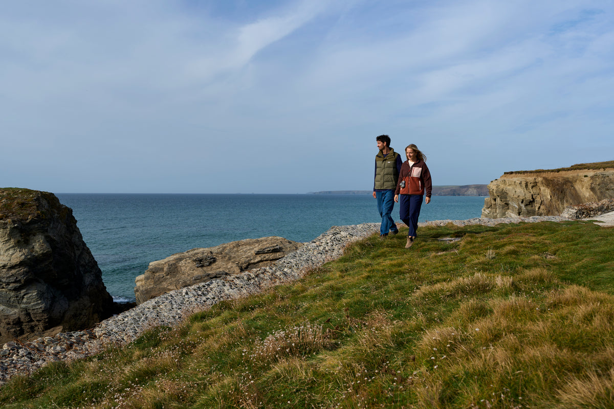 A couple walking along a grassy coastal path overlooking the sea and cliffs