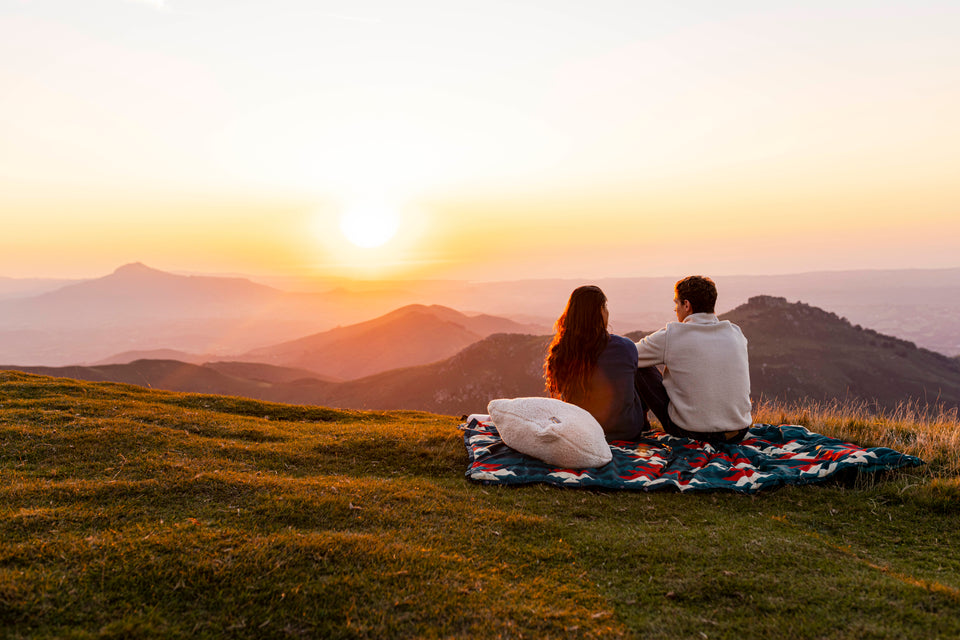 Couple sitting on a blanket watching the sunset over mountains
