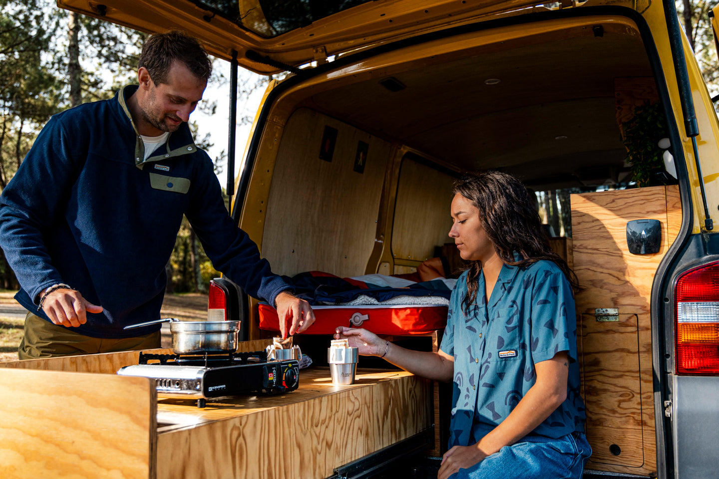 Two people preparing food in the back of a van