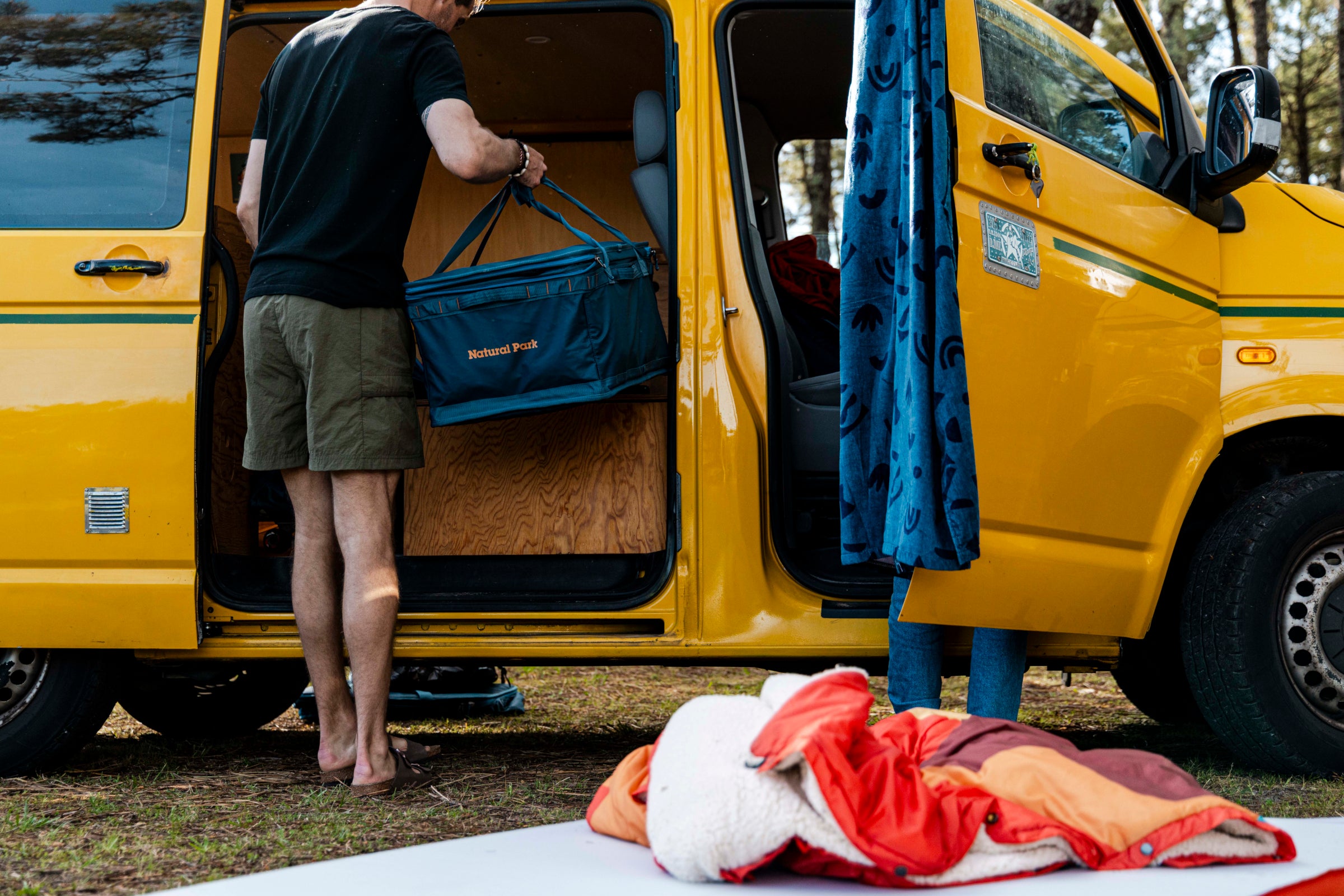 Man in shorts loading a cool bag into a camper van