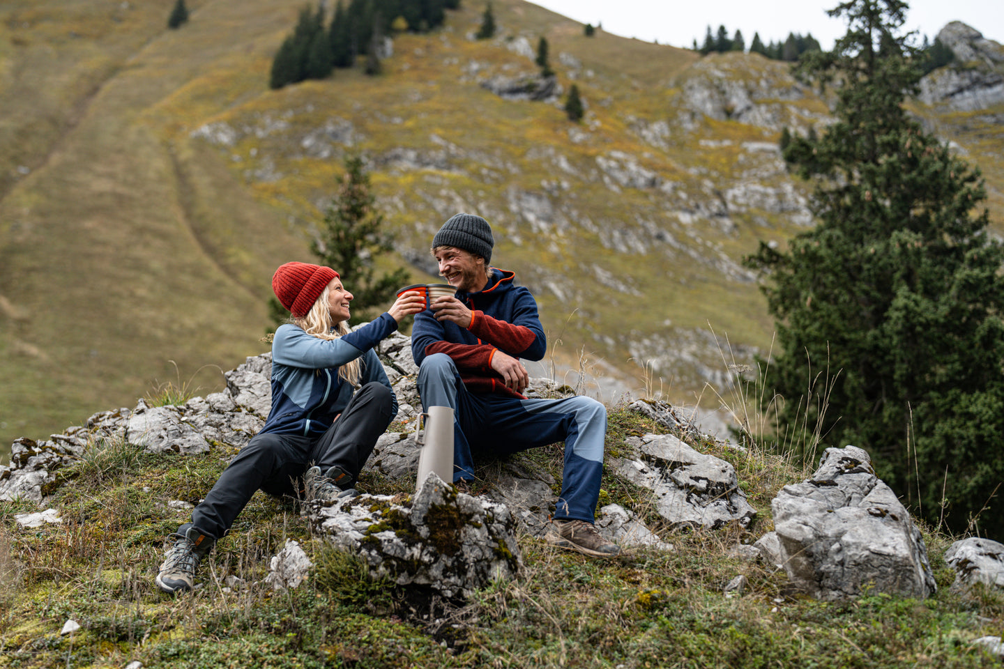 Couple sitting on rocks in the mountains wearing fleeces and beanies