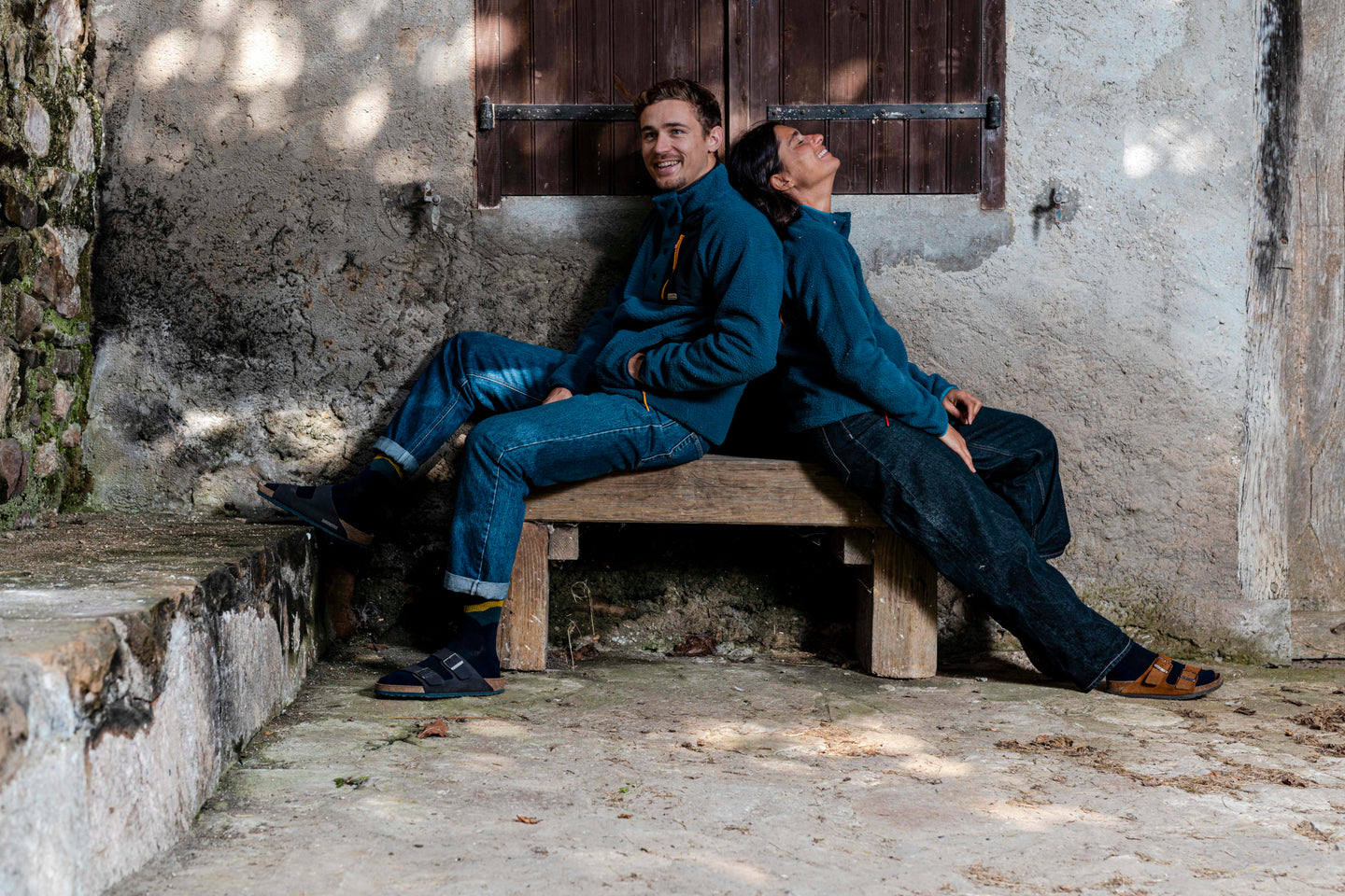 Two people sitting back to back on a wooden bench wearing blue fleeces