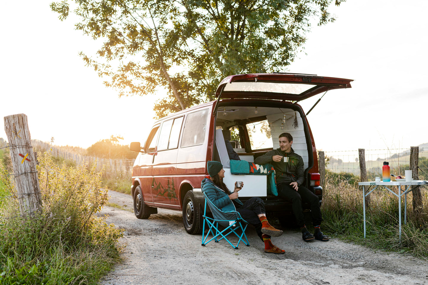 Two people relaxing beside a camper van at sunset
