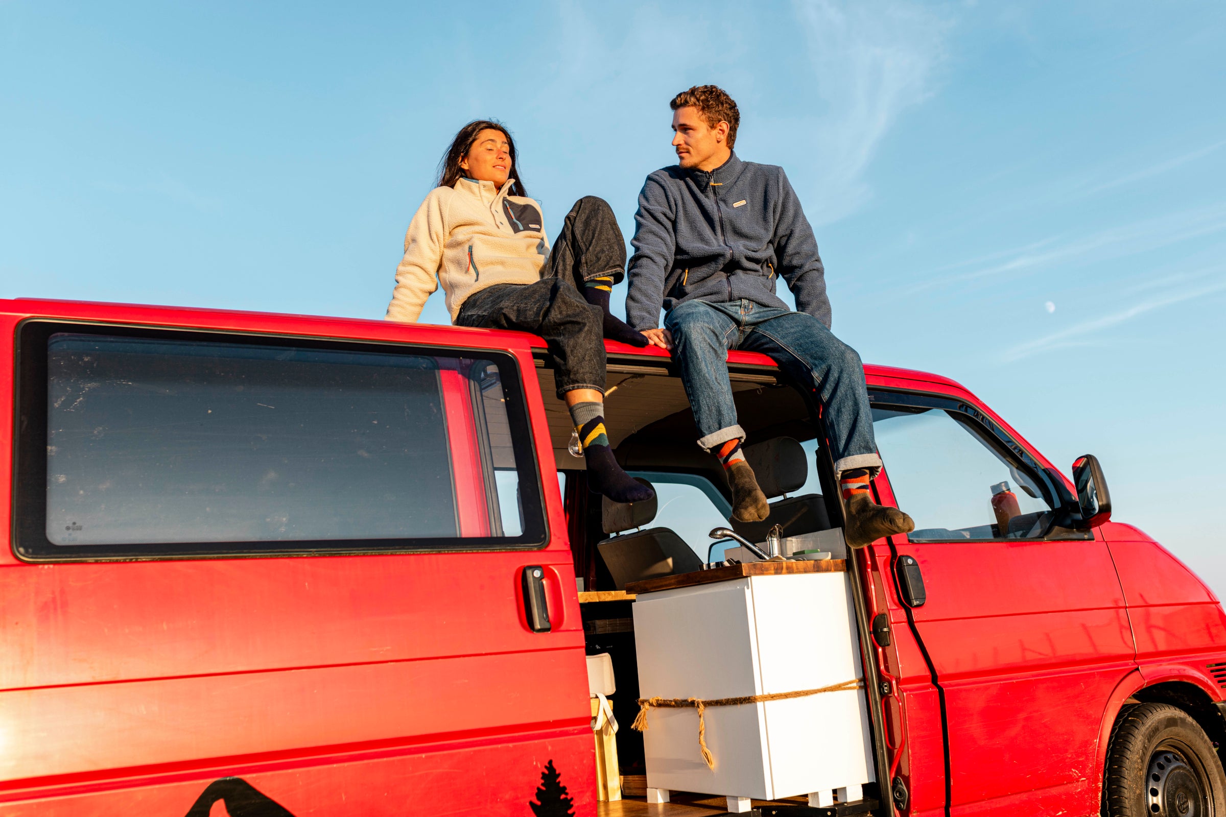 Two people sat on top of a campervan during a sunset