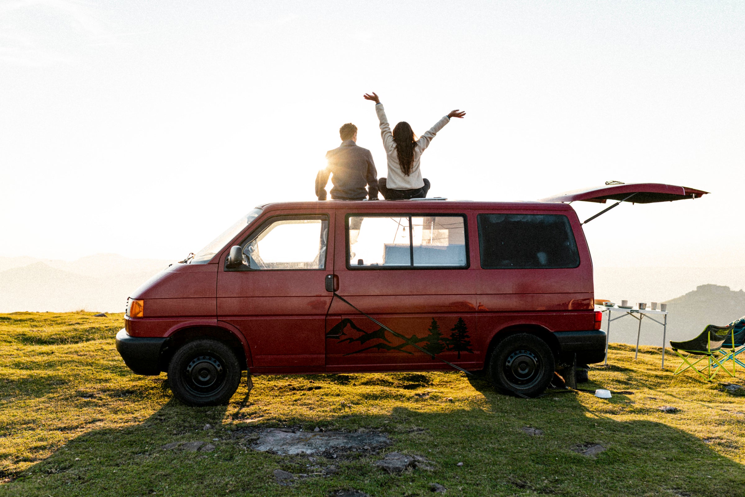 Two people sitting on top of a red camper van at sunset