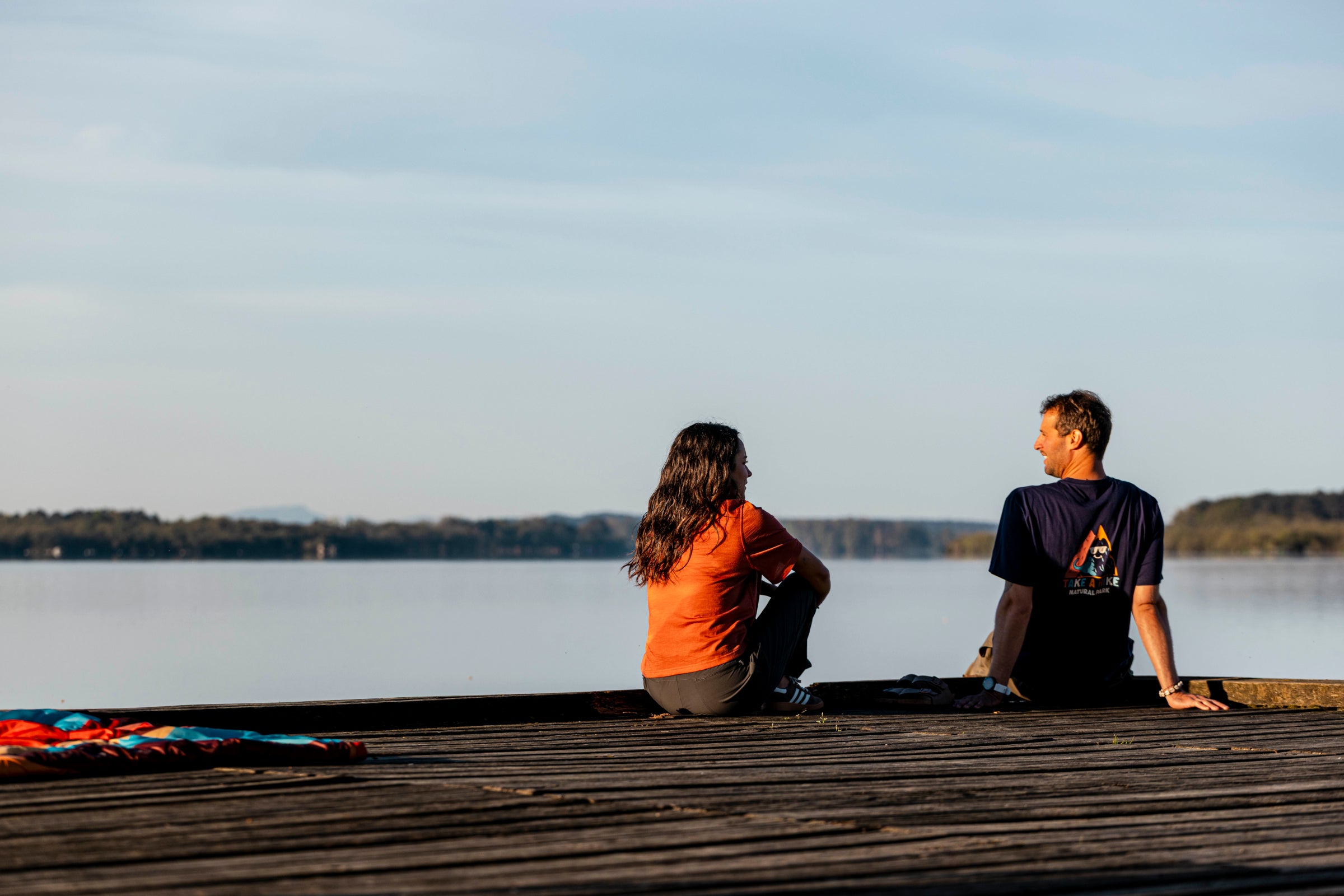 Two people sitting on a dock by a lake