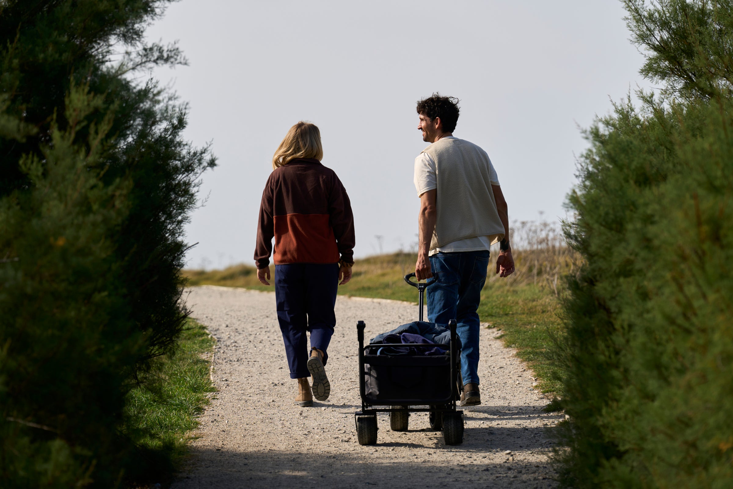 A man and a woman walking on a gravel path between green trees
