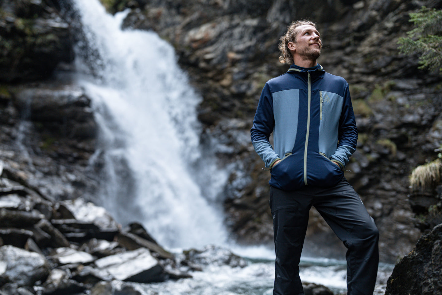 Man standing near a waterfall wearing a blue fleece jacket