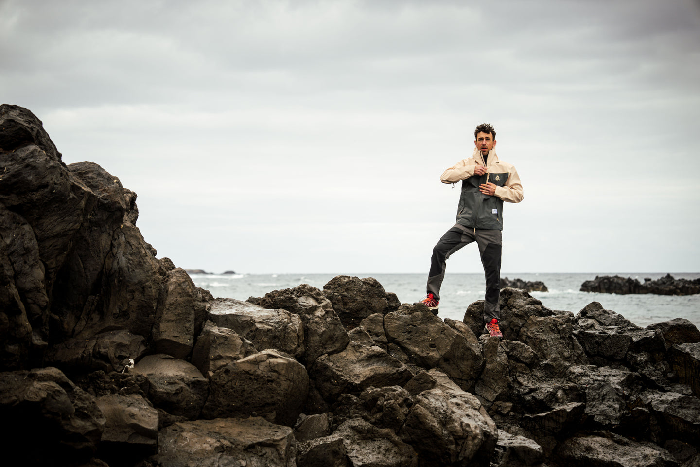 Man wearing a Natural Park waterproof jacket standing on rocks by the sea