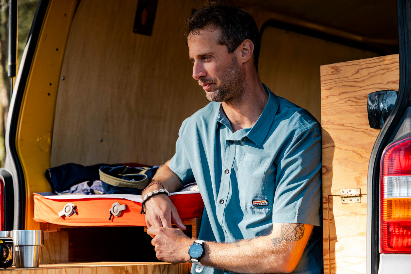 Man wearing a Natural Park shirt at the back of a campervan
