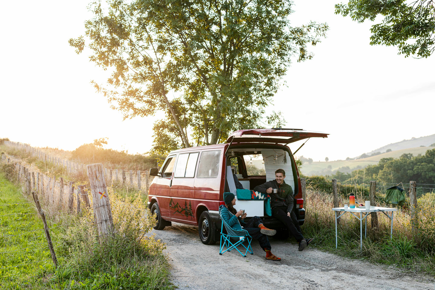 Two people relaxing beside a camper van in the countryside at sunset