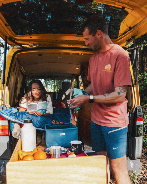 Two people in a van with camping gear and food items