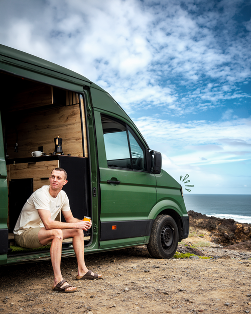Man sitting in the doorway of a green camper van by the ocean