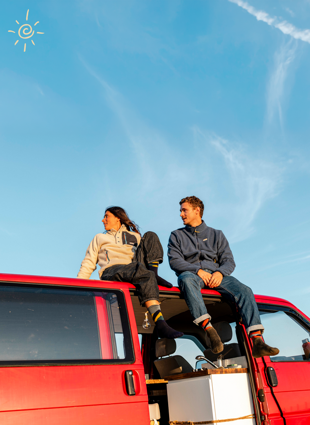 Two people sitting on the roof of a red vehicle against a blue sky