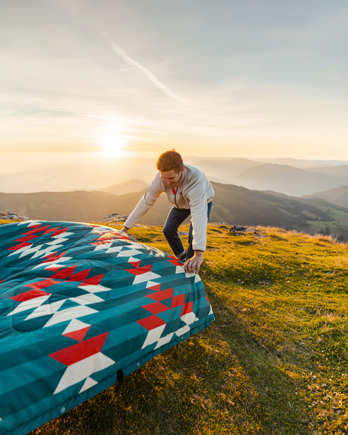 Person setting up a colorful blanket on a grassy hill