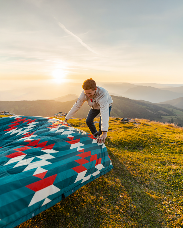 Person setting up a colorful blanket on a grassy hill