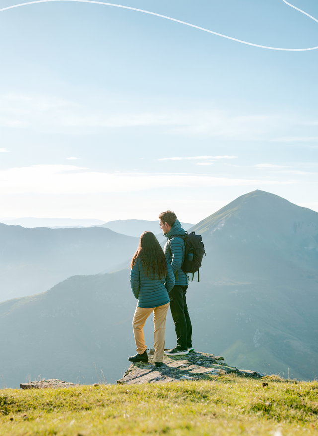 Two people standing on a mountain top with a scenic view of mountains in the background