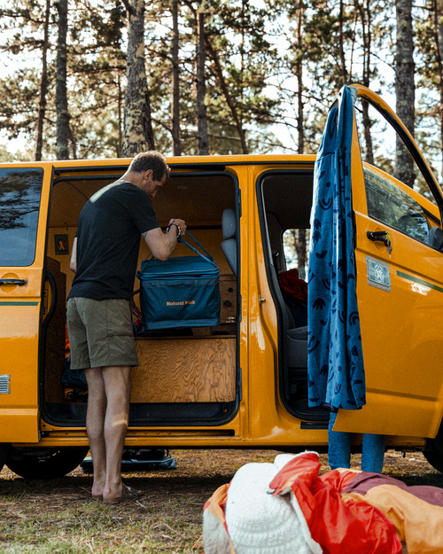 Person loading a gear box into the back of a yellow campervan