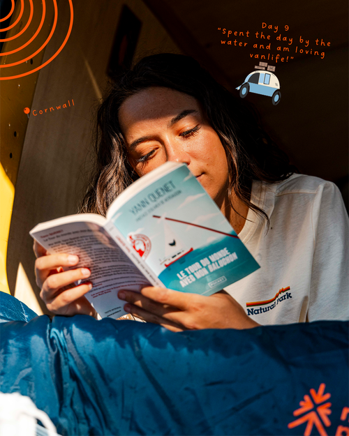 A woman in a white t-shirt reading a book in a cosy, warmly lit camper van