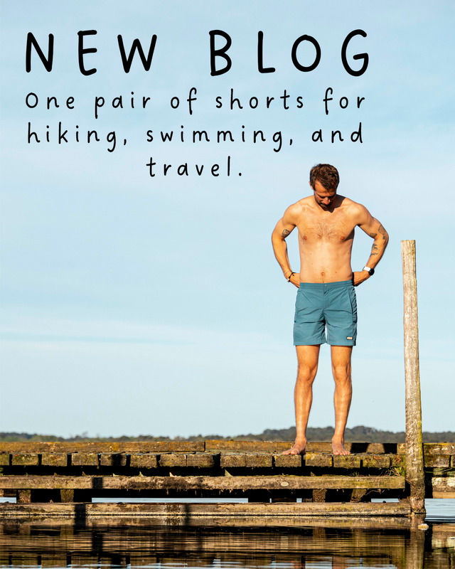 A shirtless man wearing teal-blue shorts stands on a wooden dock over calm water