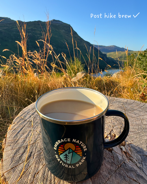 A navy enamel camping mug sits on a weathered log outdoors
