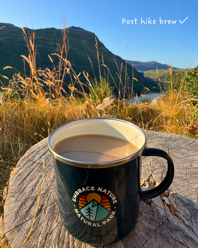 A navy enamel camping mug sits on a weathered log outdoors