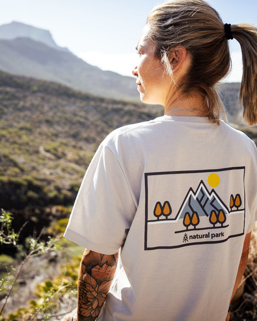 Person wearing a white t-shirt with a nature-themed design in a mountainous landscape