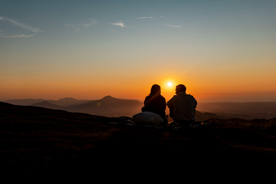 Two people sitting on a hillside watching the sunset over mountains