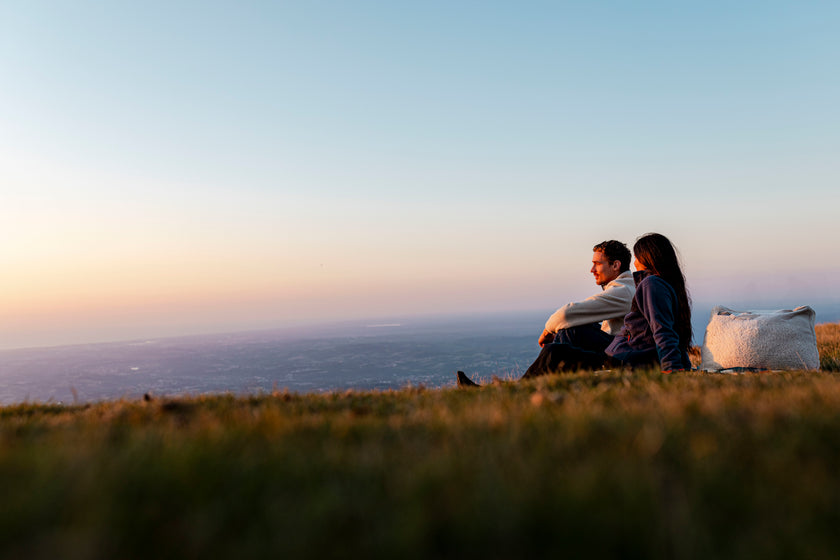 A couple sitting on a hillside at sunset