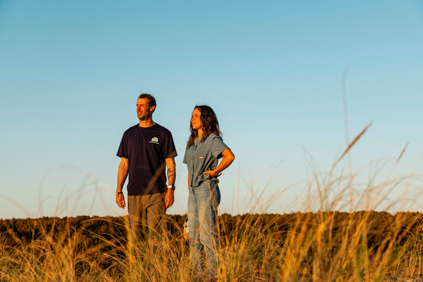 Couple wearing Natural Park shirts standing in coastal grassland
