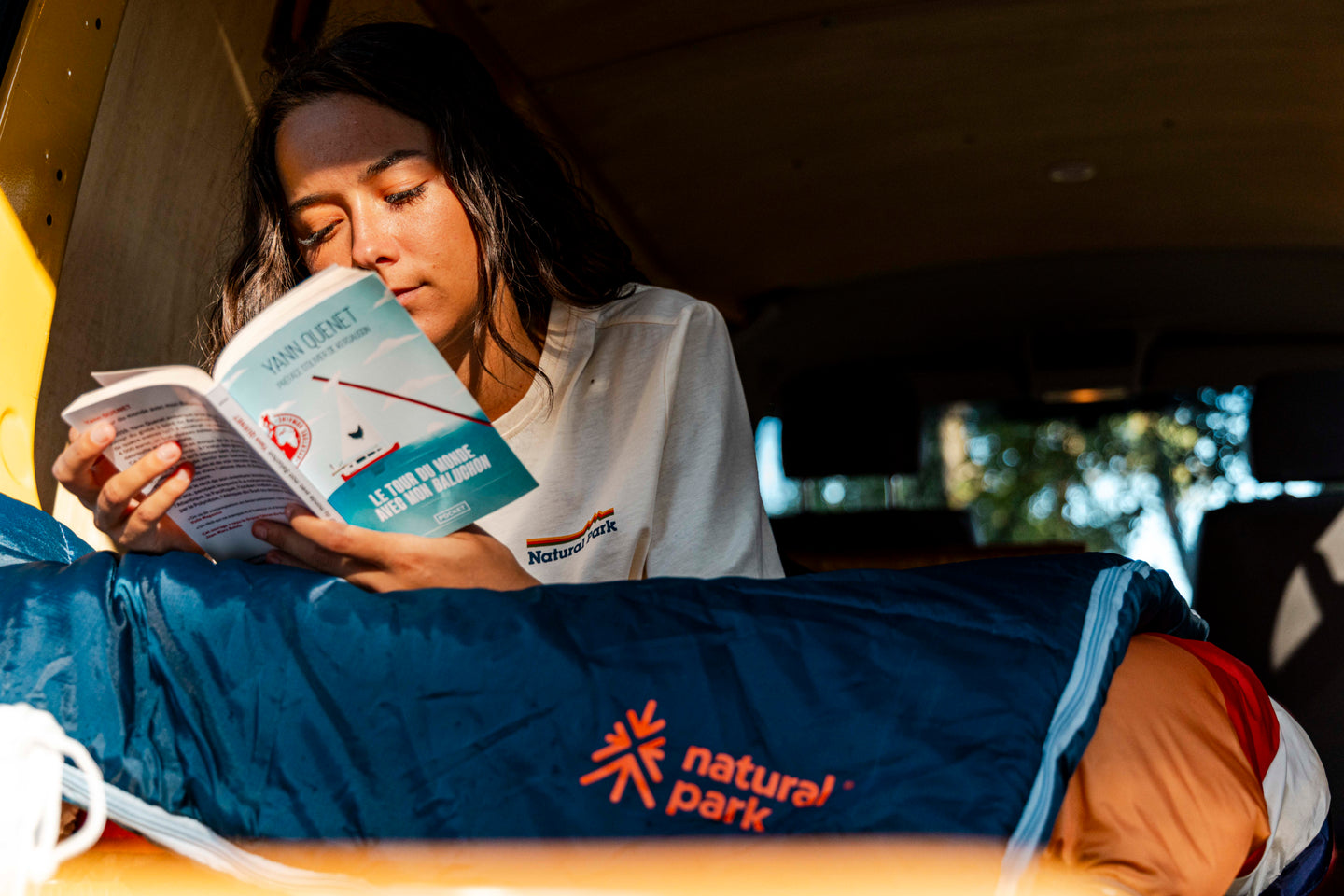 Person reading a book in a vehicle with a sleeping bag