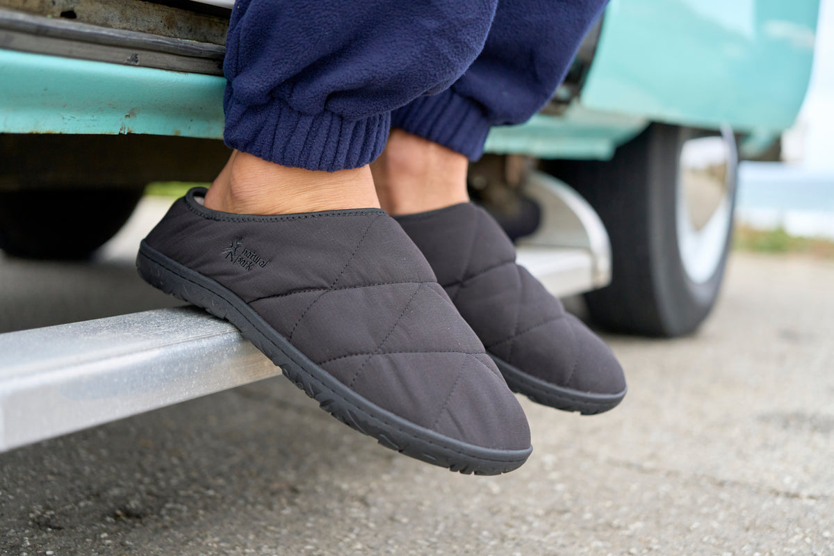 A close-up of a person wearing dark gray quilted slippers