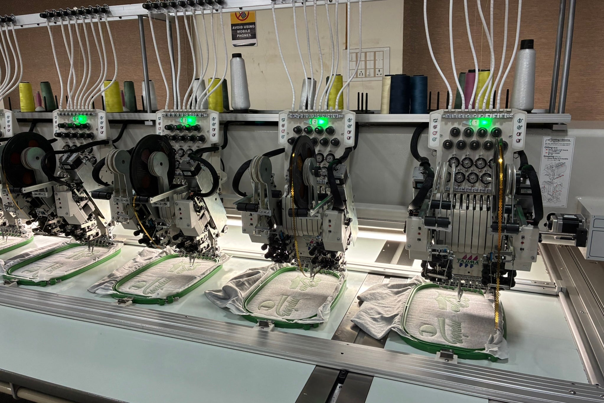 Row of industrial embroidery machines stitching logos onto fabric in a factory
