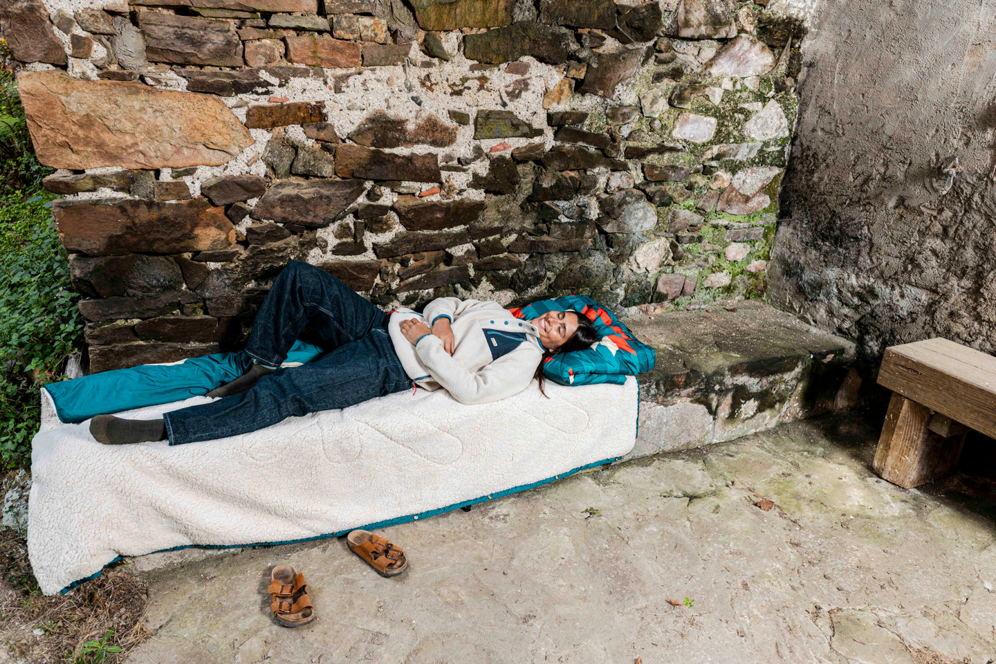 Woman lying on an outdoor bed using a colorful blanket as a pillow