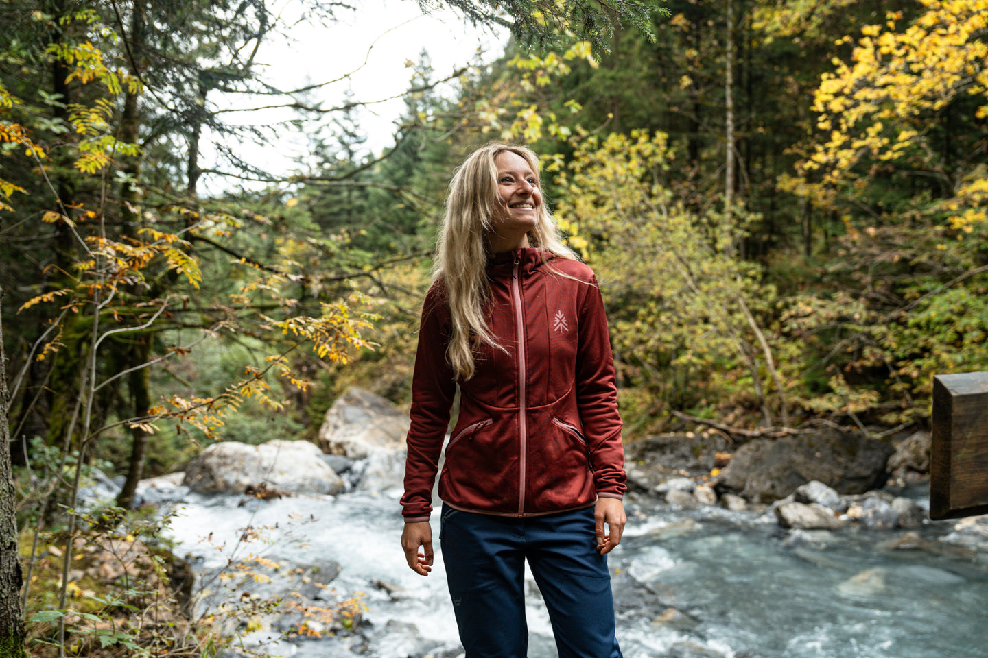 Woman standing by a forest river wearing a red fleece jacket