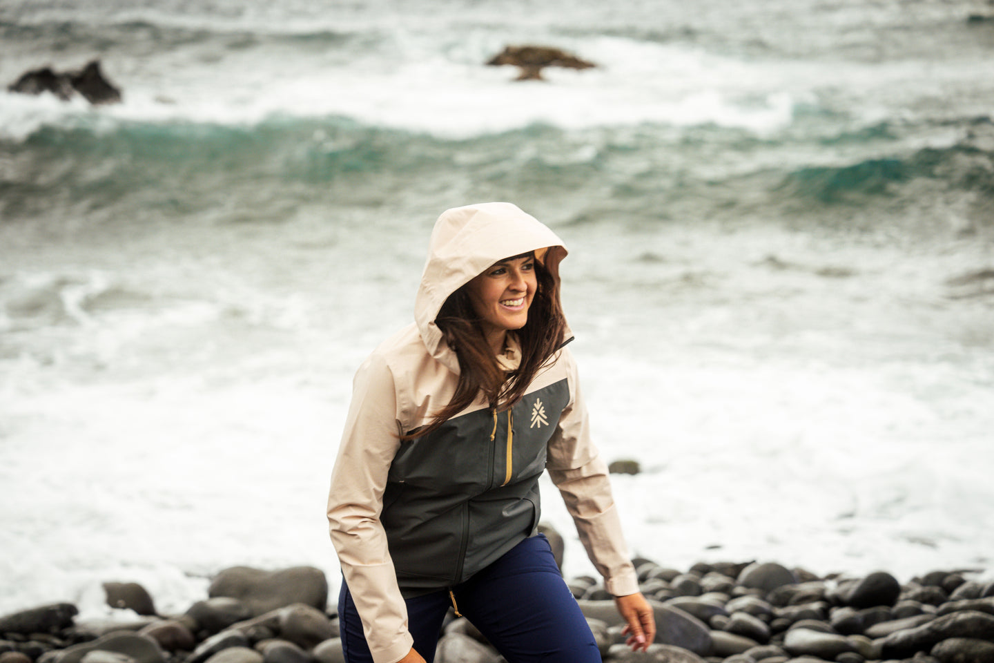 Woman smiling on a rocky beach wearing a waterproof jacket