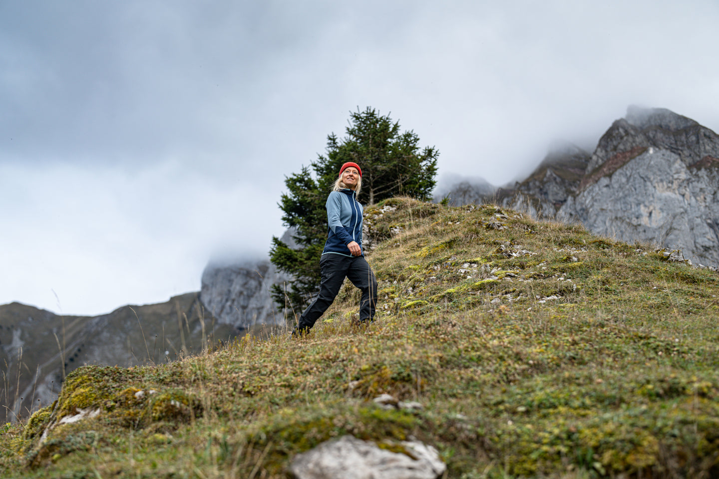 Woman hiking in the mountains wearing a blue jacket and red beanie