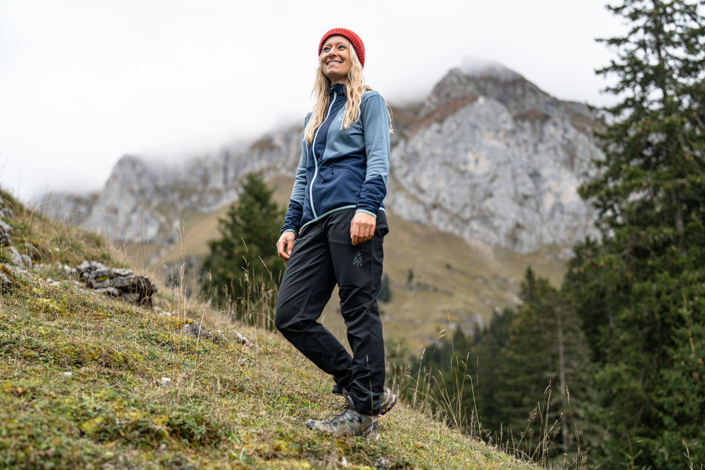 Woman hiking uphill in dark outdoor trousers and blue jacket