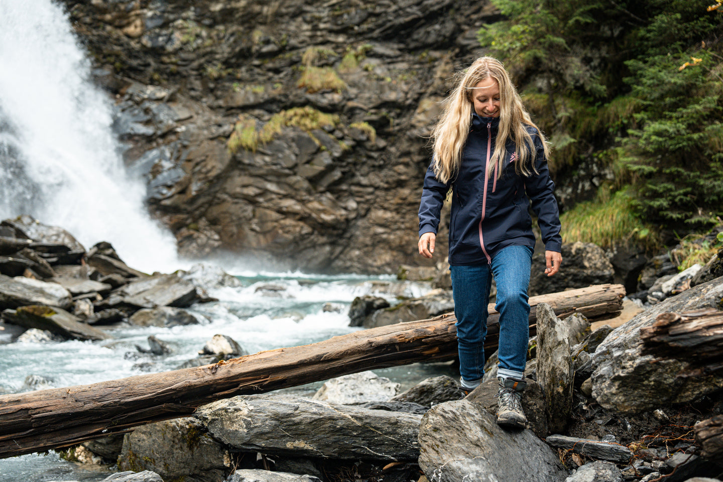 Woman walking on rocks near a waterfall wearing a waterproof jacket